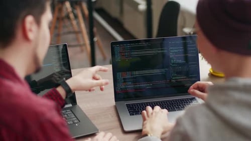 Two Hipster Coworkers Sharing Ideas About Project Sitting with Laptops in Spacious Open Space Office