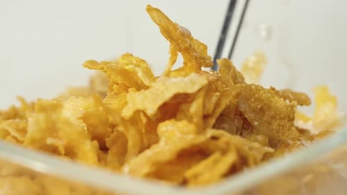 Spoon grabs yellow cornflakes with white milk from transparent bowl on a white background. Close up