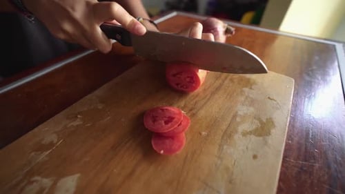 Hands slicing a tomato on a cutting board