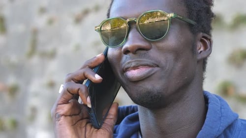 close up on smiling african man wearing sunglasses talking oh his phone