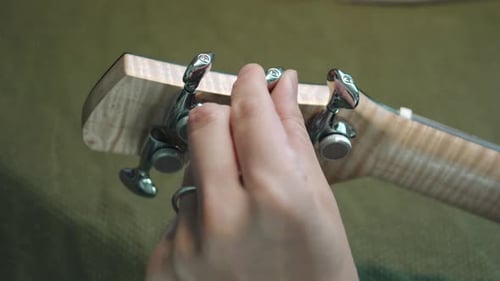 Man Checking And Tuning The Guitar By Turning The Machine Heads Of An Acoustic Guitar. - close up s