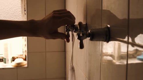 Hand Turns On Shower Faucet In Tiled Bathroom