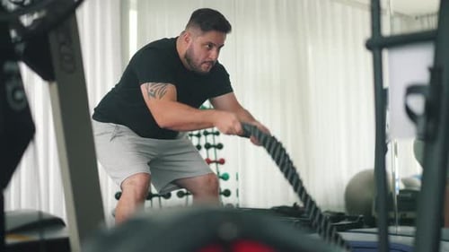 Young Man Double Whipping Exercise with battle ropes in a Gym