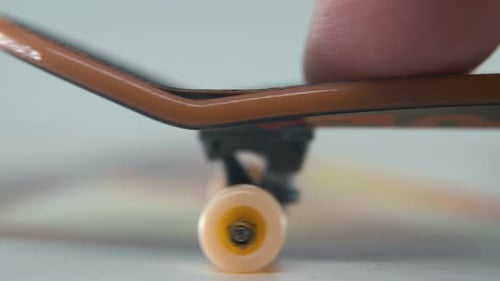 A hyper close-up detailed shot of a mini skateboard, tiny white wheels, riding fingerboard from righ