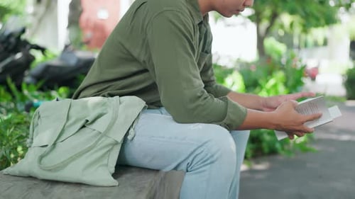 Nahaufnahme eines Mannes, der in einem Park im Freien sitzt und ein Buch liest. Gebräunter asiatischer Mann in Grün