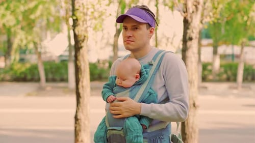 Young Father with His Newborn Baby in a Sling in the Park