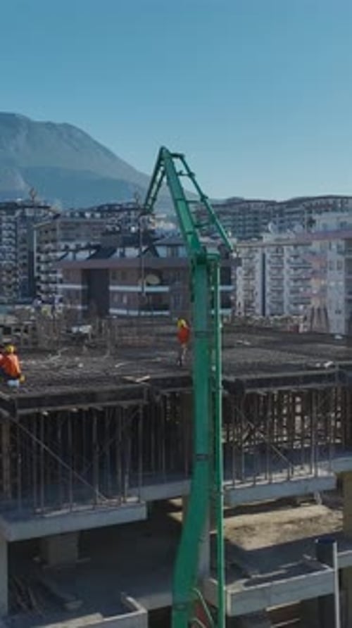 Vertical Video of Workers Pouring Concrete While a Crane Installs Structural Metal Beams on Site