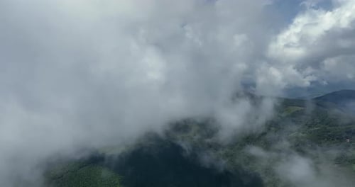 Flying trough white fluffy clouds above green mountain peaks. Beautiful summer sunny day on the high
