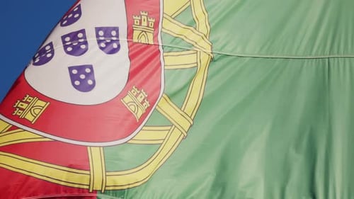 Portuguese flag waves in wind against bright blue sky