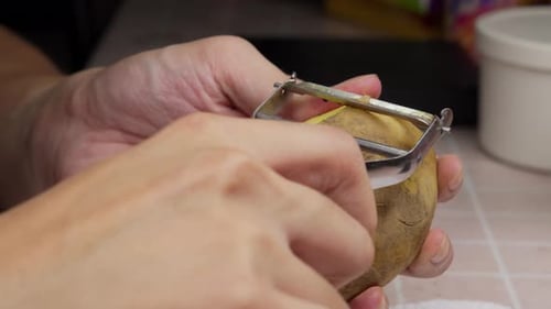 Man peeling a potato with a peeler in the kitchen. Close-up