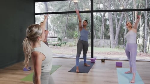 Focused diverse women stretching together on mats in yoga class with female coach, slow motion