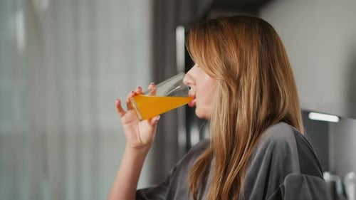 Side View of Lady Drinking Juice in Modern Kitchen with Natural Light