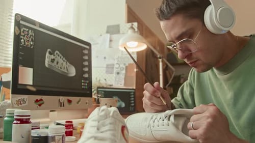 Man Painting Designs on White Sneakers at Desk