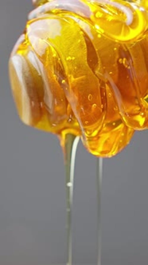 Goldener Honig tropft vom Holzlöffel in ein glänzendes Glas auf einem rustikalen Tisch