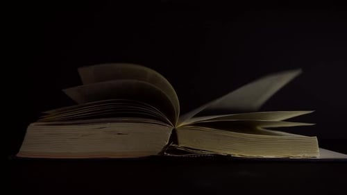 Slow motion, close up of an old, vintage, open book with pages turning on the wind, with glowing spa