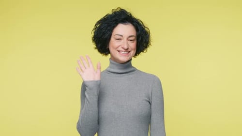 Reife Frau mit kurzem Haarschnitt winkt positiv mit der Hand und sagt Hallo, mein Freund