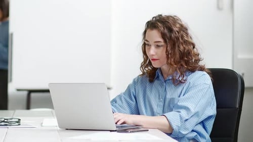 Junge Geschäftsfrau sitzt am Schreibtisch und arbeitet am Laptop