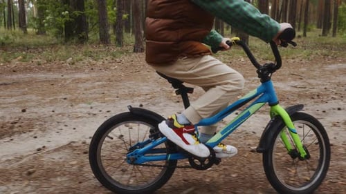 Child Pedaling Bicycle on Forest Road in Summer Day