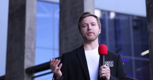 Professioneller Journalist mit Mikrofon in der Nähe eines Gebäudes im Freien