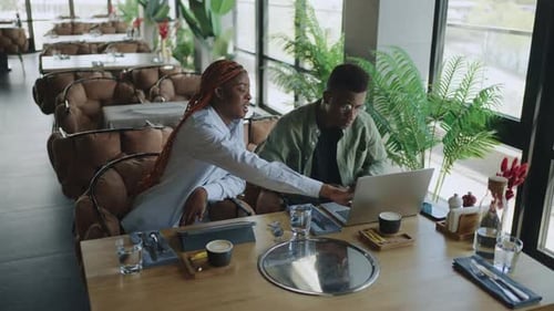 Focused Black Male and Female Professionals Collaborating on Important Project in Trendy Cafe