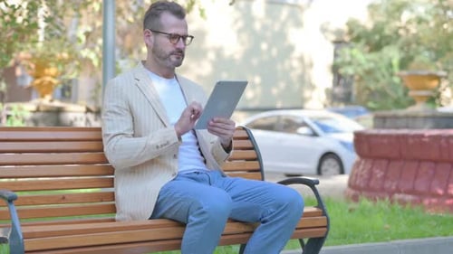 Man Using Tablet on Bench in City Park