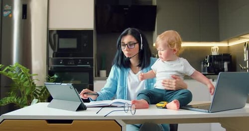 Joven empresaria seria sentada junto a la mesa de la cocina frente al portátil escribiendo mientras trabaja