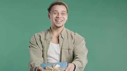 Stylish Excited Man Holding Gift Box And Gives It By Hands To Camera on Green
