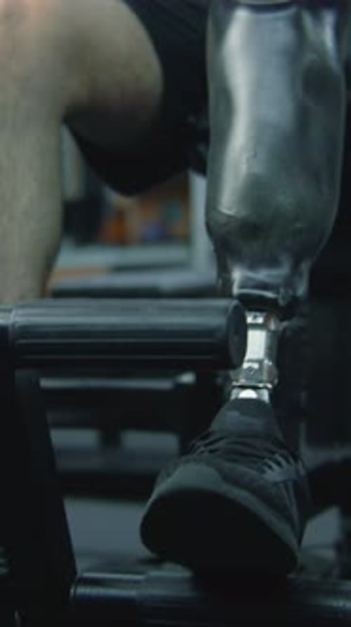 Athlete with Prosthesis on Leg Trains on Machine in Gym