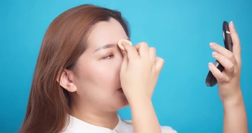 Close Up of Asian woman applying powder face for wellness skin care on blue background. Slow Motion
