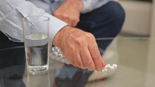 Hand Counting Small White Pills Next to Water