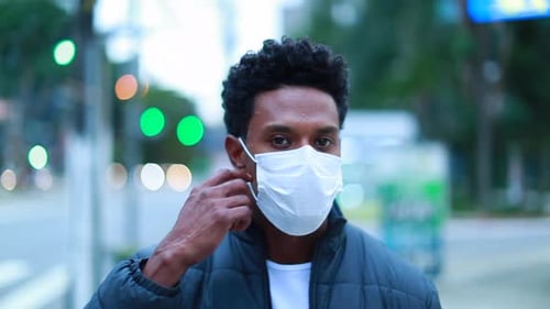 African man walking in city wearing covid mask. Black person removing outbreak mask looking to