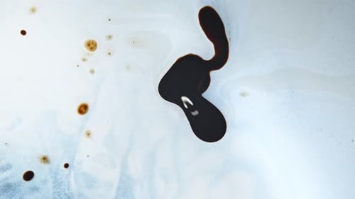 Dark liquid swirls and mixes with lighter fluid on a white surface in an abstract pattern