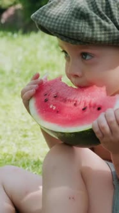 Cute Child Eating Watermelon Outdoors in Green Field