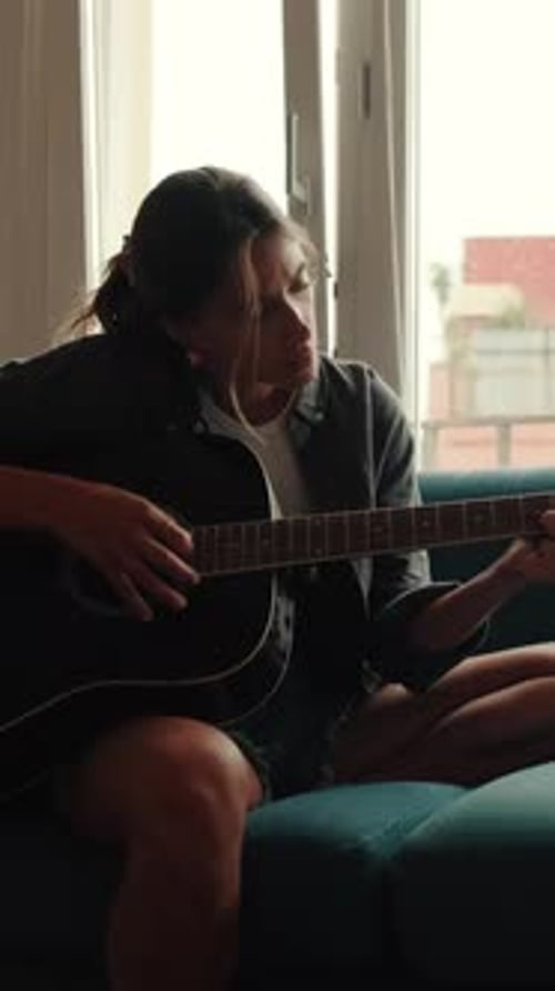 Woman Plays Guitar Indoors on Couch