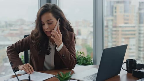 Smart brunette businesswoman talking on telephone in modern office workplace