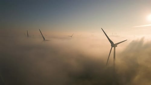 Cinematic aerial view of wind turbines in the misty sky at sunrise