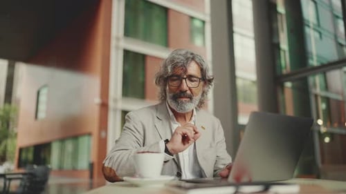 Mature businessman wearing gray jacket sits on cafe