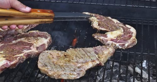 A Juicy Beef Steak is Grilled Over a Fire of Coals on an Iron Grill Resulting in a Smokey Flame That