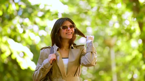 A Woman Wearing Sunglasses and a Brown Coat is Walking Down a Path