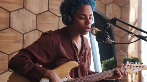 Young African American Woman Singer with Guitar Sits in Recording Studio