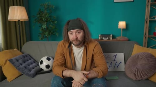 A Middleaged Man Sits on a Couch Looking at a Camera Like a TV He Eats Chips Plays Boredom