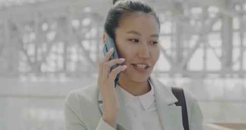 Successful Asian Employee Discussing Business on Mobile Phone Inside Modern Glass Wall Office Center