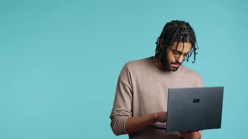 Man Inputting Data on Laptop While Standing in Blue Studio Background