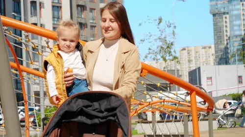 Beautiful mother holding her baby son walking on the street and pushing baby stroller