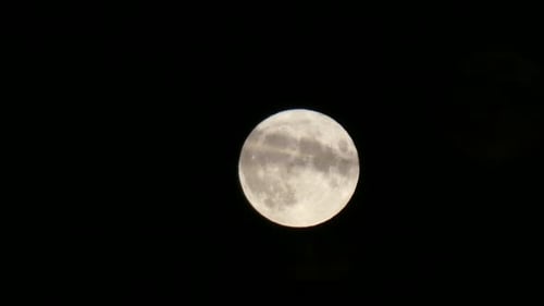 Full harvest moon crater surface closeup passing across dark sky cloud in foreground