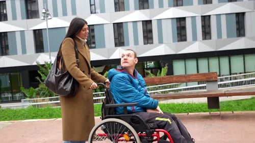 Woman Pushing Man in Wheelchair Outside Building