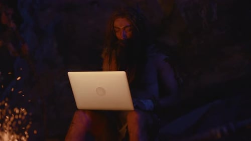 A Caveman Using a Modern Laptop in a Uniquely Primitive Setting Blending Two Worlds Together
