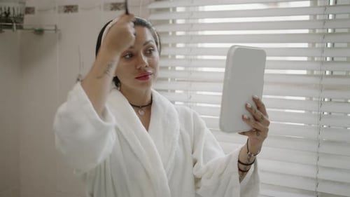 Woman Applies Makeup in Bathroom with Handheld Mirror