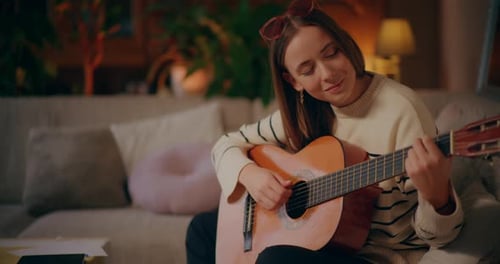 Young Woman Plays Guitar on Couch at Home