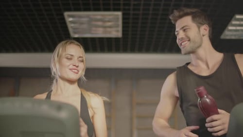 Smiling Fit Woman Giving Drinking Bottle to Man in Fitness Gym. Cheerful